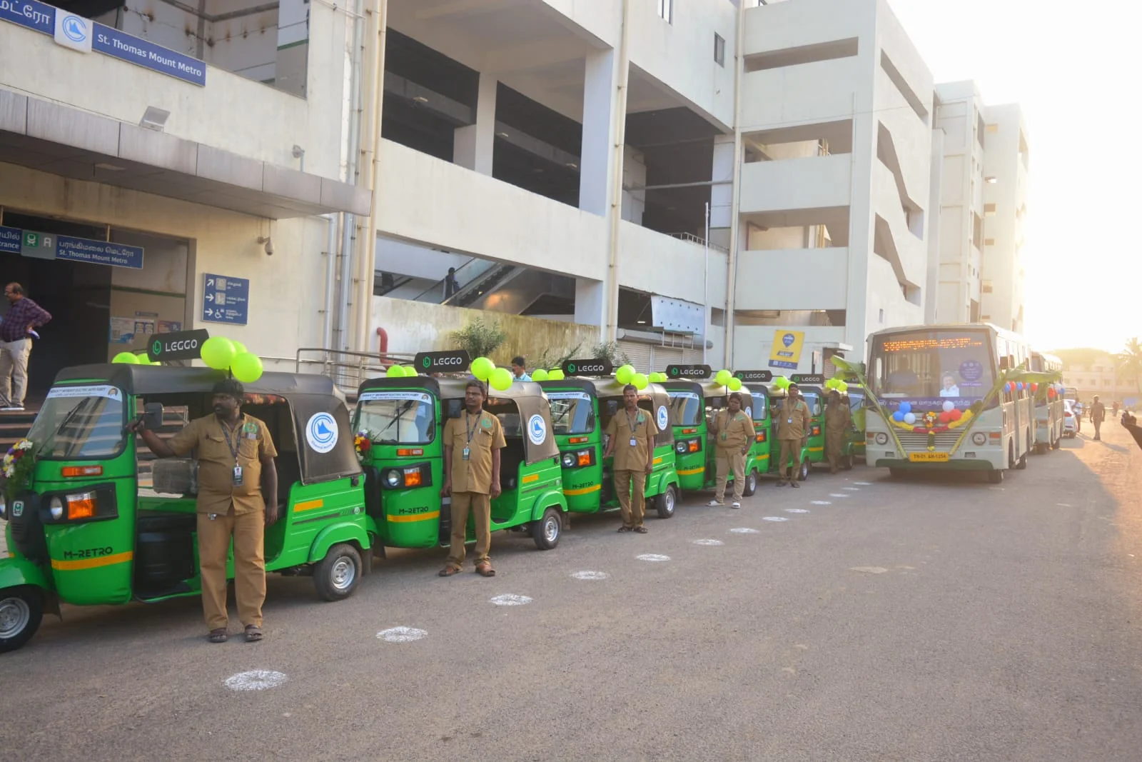 Leggo drivers in uniform beside a row of green electric autos decorated with balloons at St Thomas Mount metro station