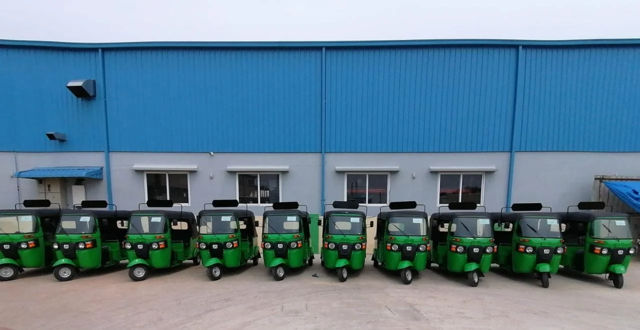Eleven green Leggo autos parked in a row in front of a blue warehouse